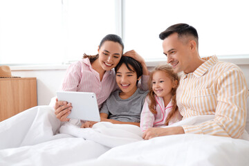 Little children with their parents using tablet computer in bedroom