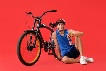 Plexiglas foto achterwand Young man sitting near bicycle and drinking water on red background © Pixel-Shot