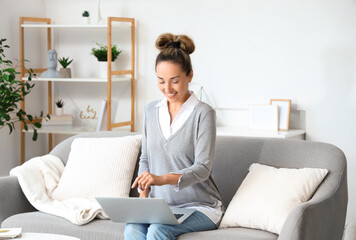 Mature woman with laptop sitting on sofa at home