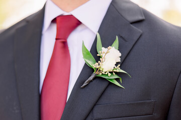Close-up of Caucasian groom's red tie with a rose boutonniere
