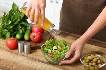 Woman adding olive oil into bowl with tasty salad at table in kitchen