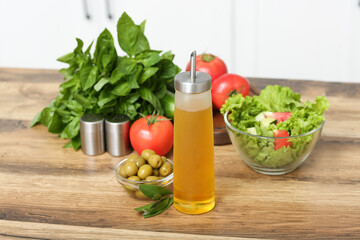 Bottle with oil, olives, vegetables and fresh salad on table in kitchen