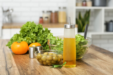 Bottle with oil, olives and fresh salad on table in kitchen
