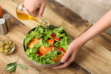Woman adding olive oil into bowl with tasty salad at table