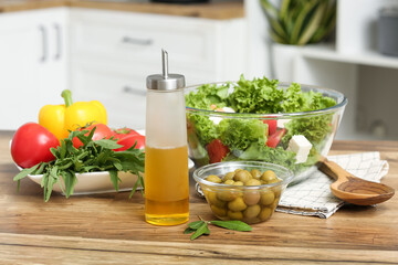 Bottle with oil, fresh salad, olives and vegetables on table in kitchen