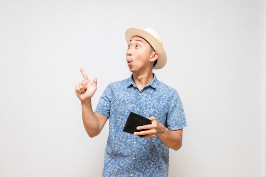 Positive asian man blue shirt wear hat holding wallet amazed gesture point finger isolated