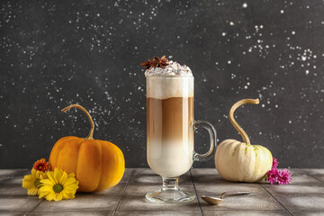 Glass cup of tasty pumpkin latte with star anise and beautiful flowers on grey tile table