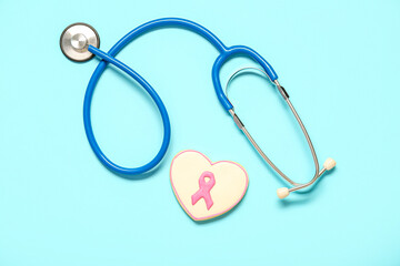 Heart shaped cookie with pink ribbon and stethoscope on blue background. Breast cancer awareness concept