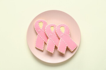 Plate with cookies in shape of pink ribbon on light yellow background. Breast cancer awareness...