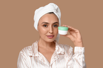 Young woman with jar of cream on brown background, closeup