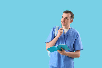 Male medical student with copybook on blue background