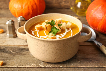 Pot of delicious pumpkin cream soup with croutons and parsley on wooden background