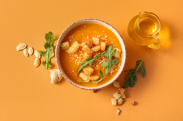 Bowl of delicious pumpkin cream soup with croutons, arugula and seeds on orange background