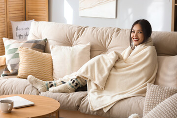 Young Asian woman with plaid sitting on sofa at home