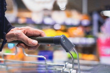 An older man's hand pushing a cart in a supermarket, blurred background with copy space