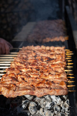 A lot of juicy meat kebabs in a row on the grill. Meat pieces strung on wooden skewers on the grill. The process of cooking kebabs with a lot of smoke. Cooking in nature
