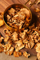 Saucepan and wooden board with tasty dried mushrooms on brown background