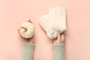 Woman with pumpkin and warm socks on beige background