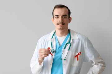 Fototapeta premium Young male doctor with red ribbons on grey background. World AIDS Day concept
