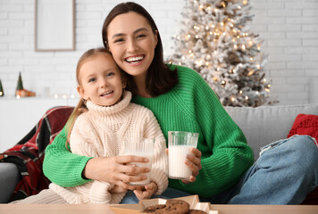 Happy mother and her little daughter drinking milk at home on Christmas eve