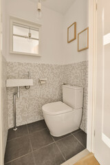 Fototapeta na wymiar a white toilet in a small bathroom with grey tiles on the walls and floor to the right is a mirror