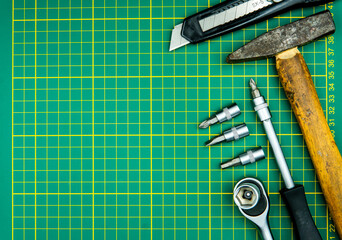 screwdriver hammer bits and knife isolated on green cutting mat