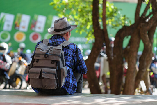 Young hipster man traveling with backpack and hat Happy solo traveler sitting in the courtyard of a landmark and popular tourist attraction. Travel, learning, lifestyle concepts.