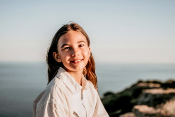 Adorable teenage girl outdoors enjoying sunset at beach on summer day. Close up portrait of smiling young romantic teenager girl with long hair on beach at summer evening. Travel and holidays