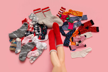 Fototapeta na wymiar Legs of young woman with pile of socks on pink background