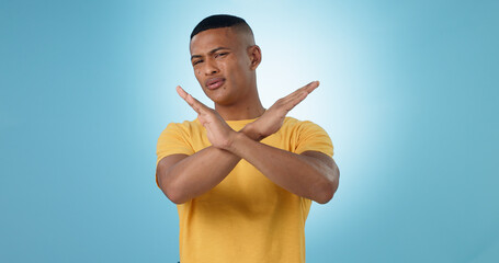 Man, cross and hands for no, portrait or studio with frustrated face for choice by blue background....
