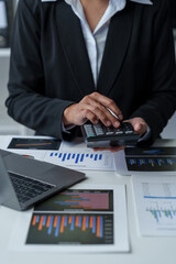 Asian businesswoman works on laptop and calculates with financial calculator from graphs,...