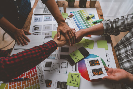 Design team, ux ui developers join hands to brainstorm on the design of mobile app interface layouts and website pages on the desktop and reach an agreement on success. Teamwork concept.