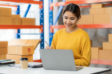 Beautiful Asian startup owner stays happily at home with packages on SME supply chain, purchasing, omnichannel purchasing or online selling ideas at home.