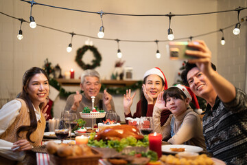 Asian family selfie Christmas dinner moment in holiday festive by father use smartphone and take photo lifestyle before enjoy eating roasted turkey and cupcake dessert in happiness home