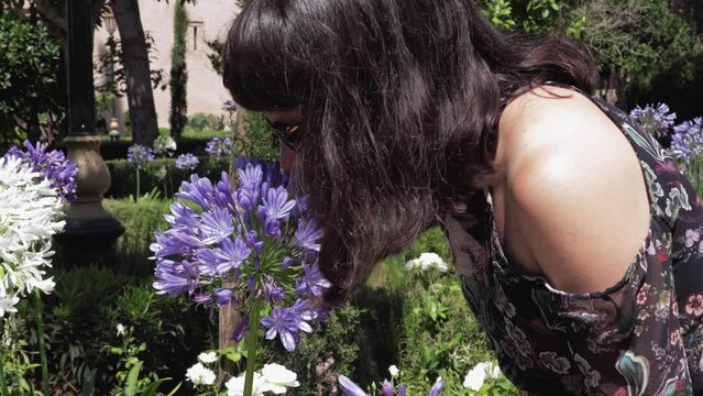 Young lady enjoying the fragrance of a blooming violet flower, during a summer day in a beautiful garden