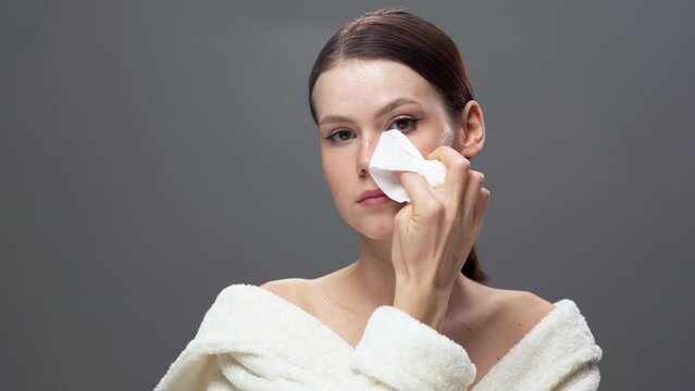 Face of young caucasian girl washing off her makeup. Young beautiful woman wipes her face skin with napkin. Skin care