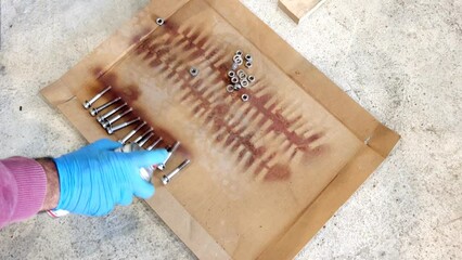 A mechanic worker hand cleaning rust from the bolts with penetrating oil lubricant spray with blue latex disposable gloves. Industrial factory employee worker hand cleaning washer nut bolt and spray - Powered by Adobe