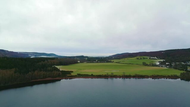 flying parallel to a large grassy meadow on the shoreline of lake Loch Ness