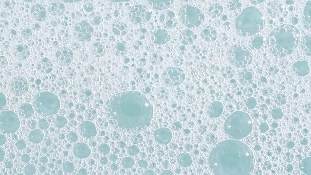 Bubbles of white soap foam on a blue background. Bathtup Soap Foam. Texture of Soap Foam Bubbles. Natural White Shampoo Bubbles Motion. High quality 4k footage