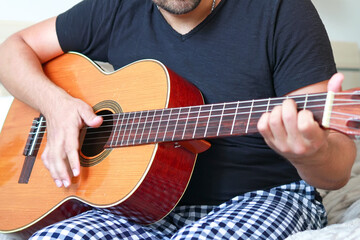 Close-up of a man playing guitar at home in his home suit.
