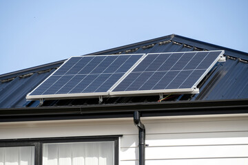 Solar panels on concrete tile roof of residential house with white wooden plank walls.
