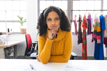 Focused biracial female fashion designer having video call at desk in studio