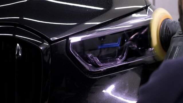 Close-up of a man polishing a headlight with a polishing machine on a car in a service station. 