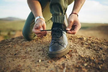 Tuinposter Hands, tie shoes and hiking in nature for travel, training or adventure outdoor. Fitness, sports and person tying laces on sneakers to start workout, walk or running, cardio or workout in countryside © Sharne/peopleimages.com