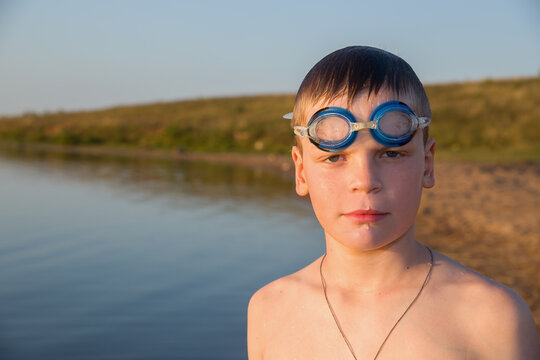 Portrait of a European boy wearing swimming goggles. In the background is the coastline of the sea.