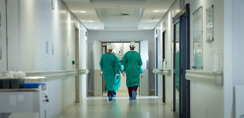 Diverse male and female surgeons wearing surgical gowns walking in corridor at hospital