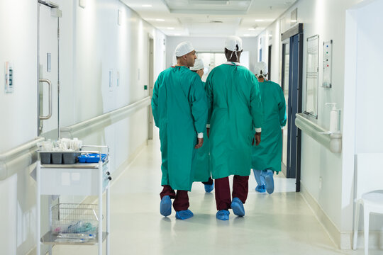 Diverse Male And Female Surgeons Wearing Surgical Gowns Walking In Corridor At Hospital