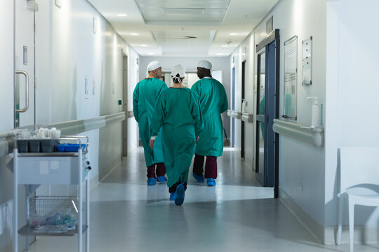 Diverse male and female surgeons wearing surgical gowns walking in corridor at hospital