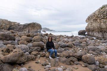 girl with sunglasses sitting on rocks by the sea on an overcast day