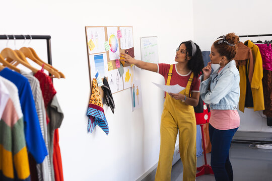 Two biracial female fashion designers discussing and looking at colour wheel in sunny studio